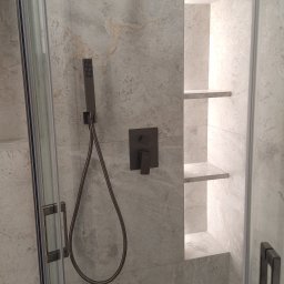 Mt Dekor - Nowoczesna kabina prysznicowa z szarymi płytkami imitującymi marmur, wnęką z półkami i czarną armaturą. Minimalistyczny design, eleganckie wykończenie.