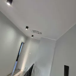 Szary korytarz z nowoczesnym oświetleniem sufitowym i kratką wentylacyjną. Minimalistyczny design, jasne wnętrze z elementami czerni.