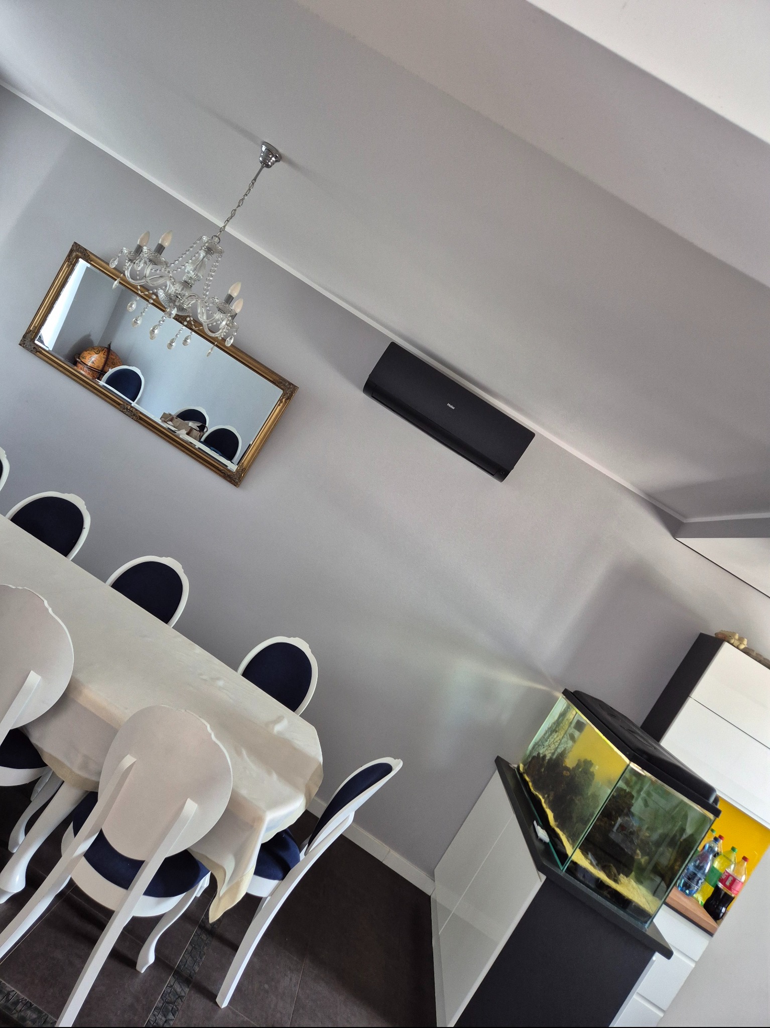 Nowoczesne wnętrze jadalni z klimatyzatorem Haier na ścianie, lustrem z kryształowym żyrandolem i akwarium. Ustawione pod kątem.