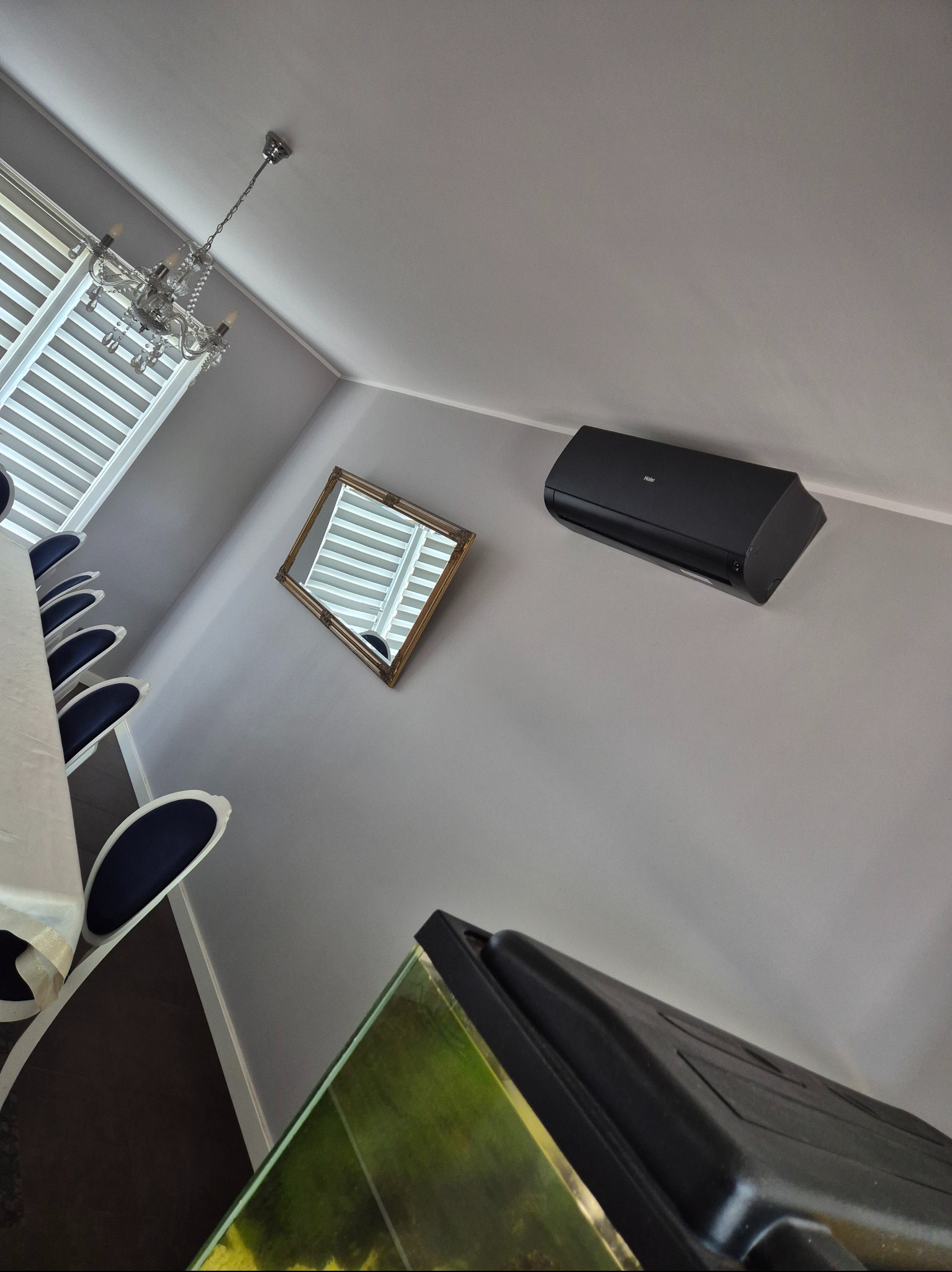 Czarny klimatyzator Haier na szarej ścianie w eleganckim wnętrzu z żyrandolem i lustrem. Widok z dołu, ukośny kadr.