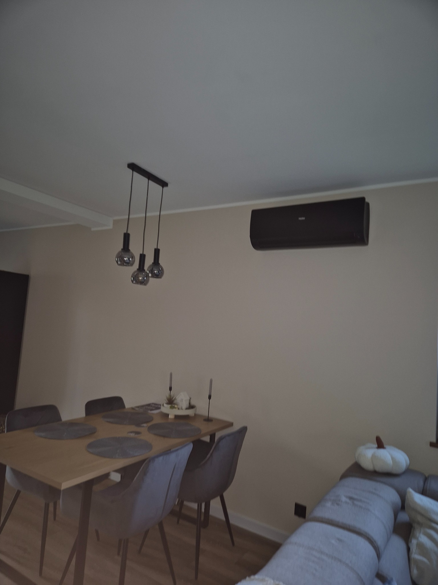 Nowoczesny, czarny klimatyzator Haier zamontowany w salonie w Wałycz, nad stołem jadalnym. Widoczne szare krzesła i dekoracje.