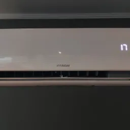 Biała jednostka klimatyzacji Hyundai zamontowana na szarej ścianie, wyświetlająca temperaturę 17 stopni.