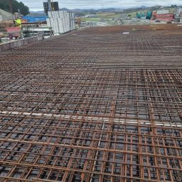 Adam Sobolewski - Siatka zbrojeniowa ułożona na deskowaniu, widok z góry, w tle krajobraz z budynkami i dźwigiem.