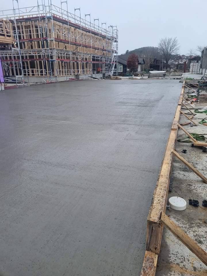 Wylany, świeży beton fundamentowy w Łodzi, z drewnianym szalunkiem i rusztowaniem budynku w tle.