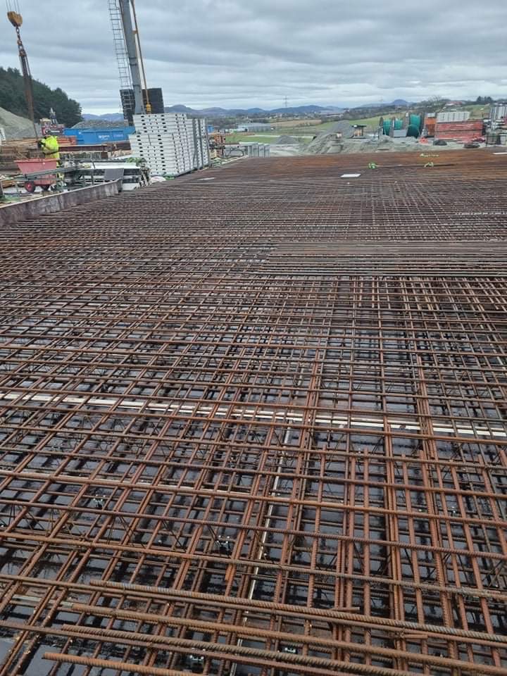 Siatka zbrojeniowa ułożona na deskowaniu, widok z góry, w tle krajobraz z budynkami i dźwigiem.