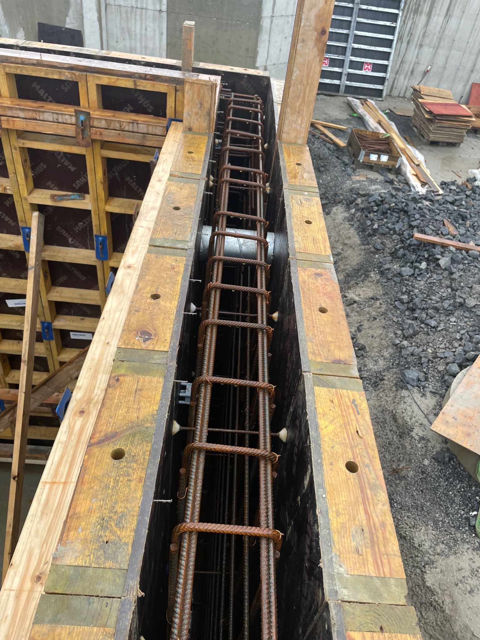 Szczegółowe ujęcie z góry na szalunek zbrojeniowy z ułożonymi prętami zbrojeniowymi wewnątrz, przygotowany do zalania betonem, widoczne drewniane elementy szalunku i rury wewnątrz konstrukcji.