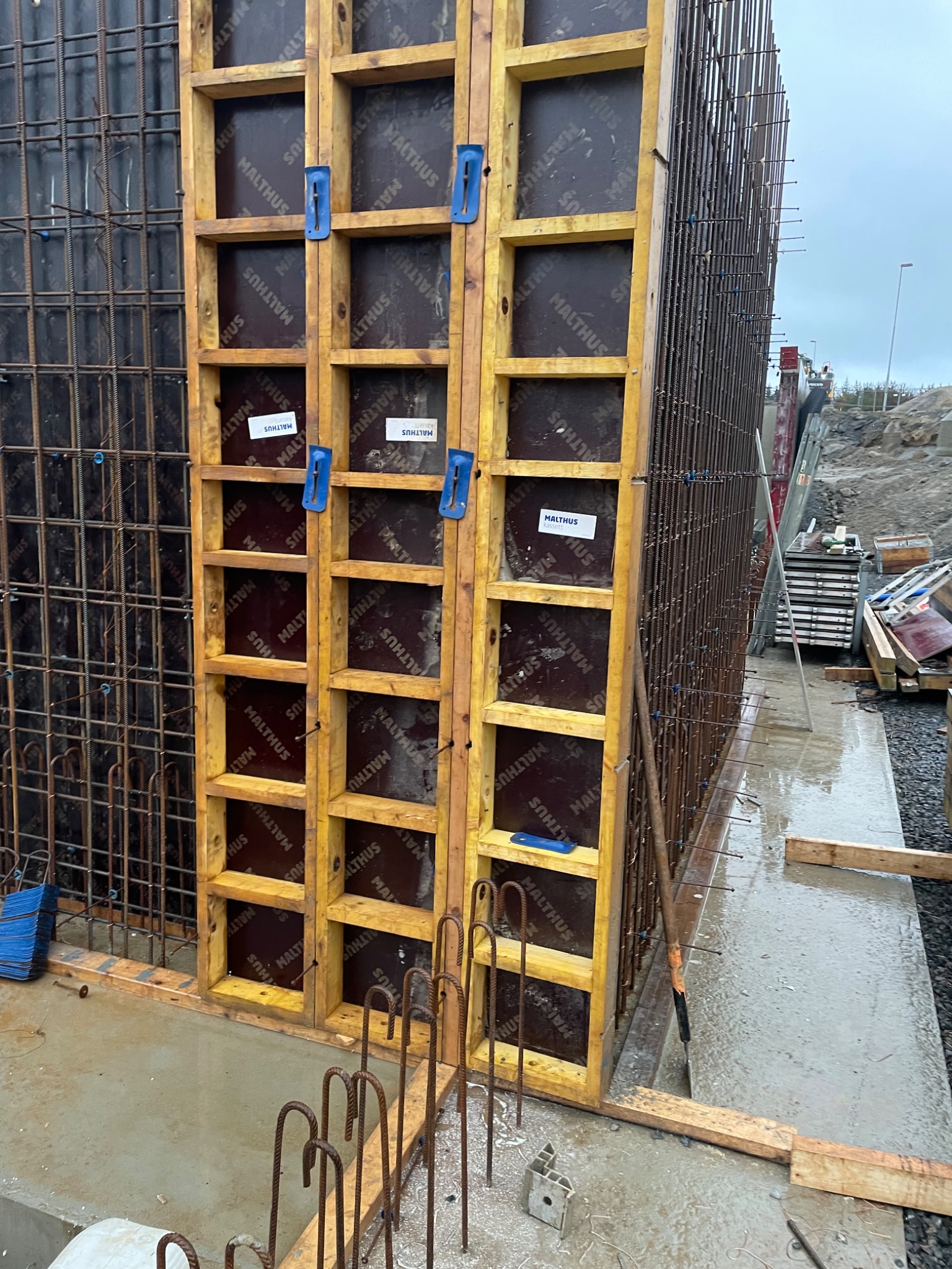 Szczegółowy widok szalunku z drewnianą ramą i metalowym zbrojeniem, przygotowany do betonowania, na mokrej powierzchni fundamentu.