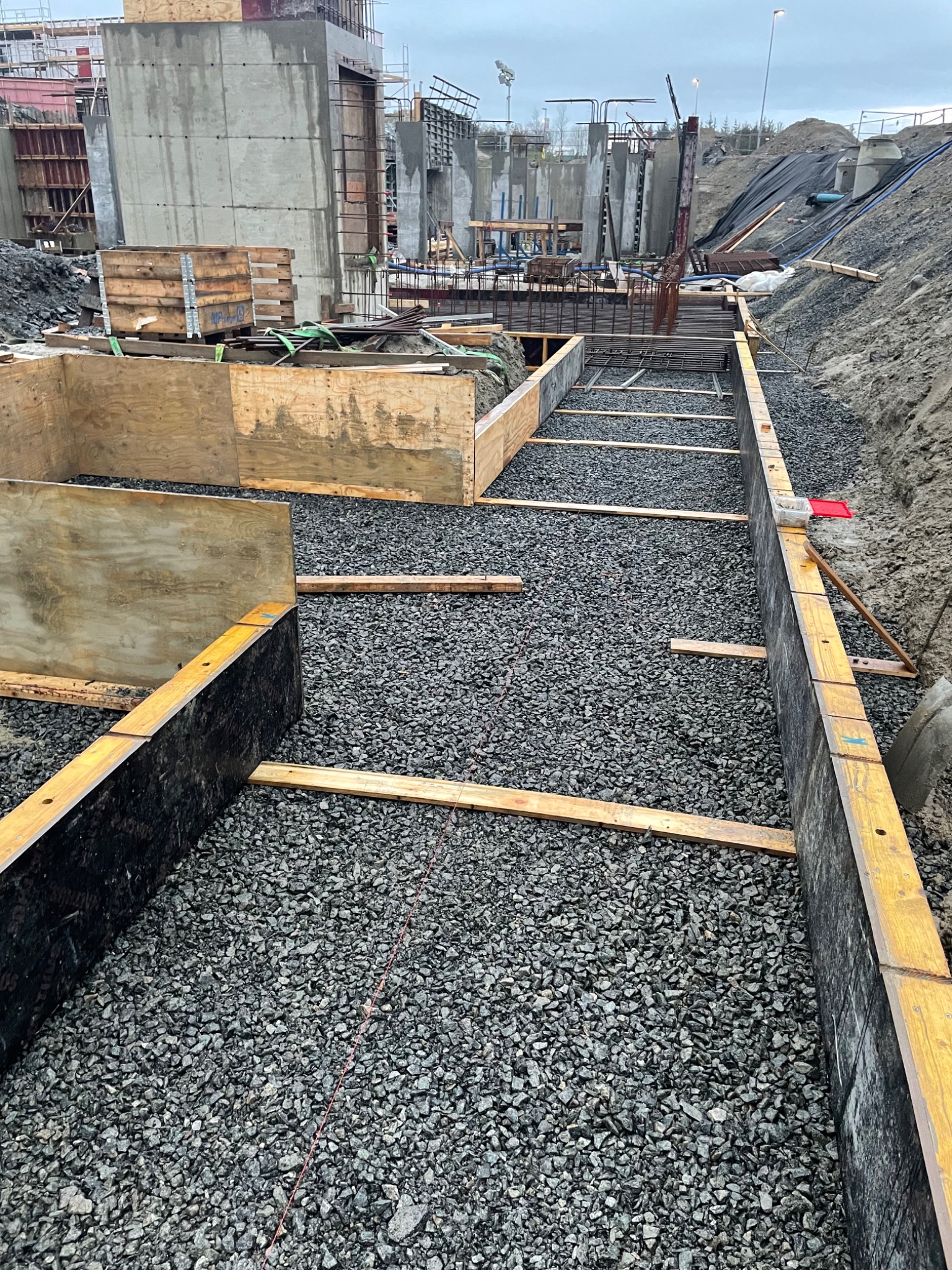 Przygotowanie wykopu pod fundamenty: szalunki drewniane, podsypka żwirowa, widoczne zbrojenia w tle.