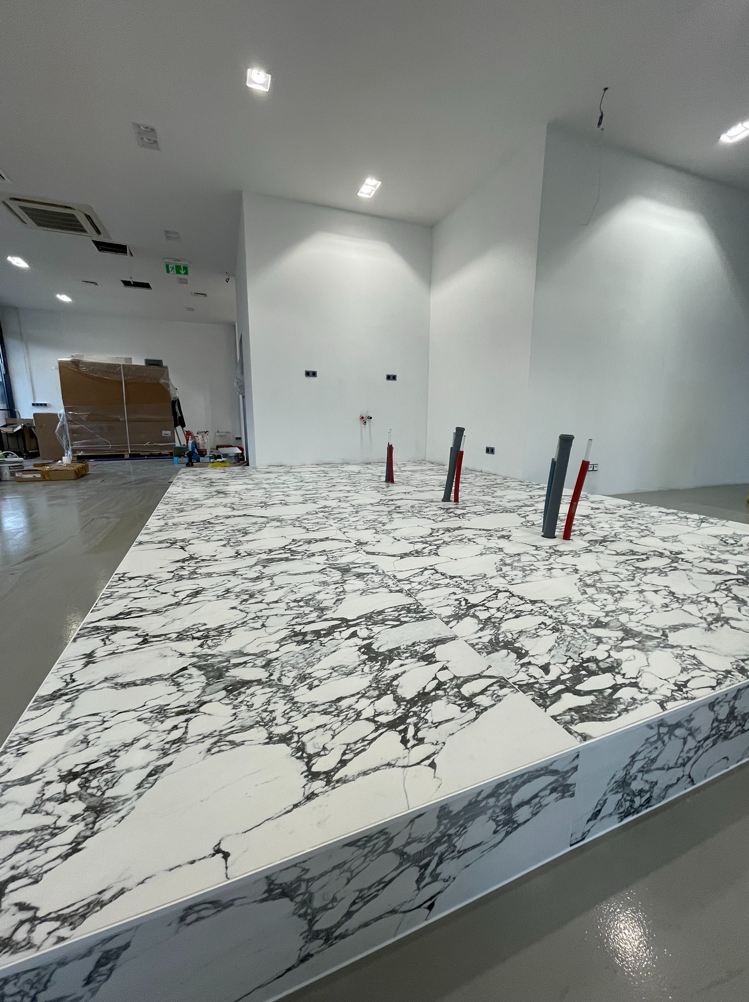 Biała marmurowa posadzka z widocznymi pionami instalacji w minimalistycznym wnętrzu. Widok z perspektywy podłogi, jasne oświetlenie.