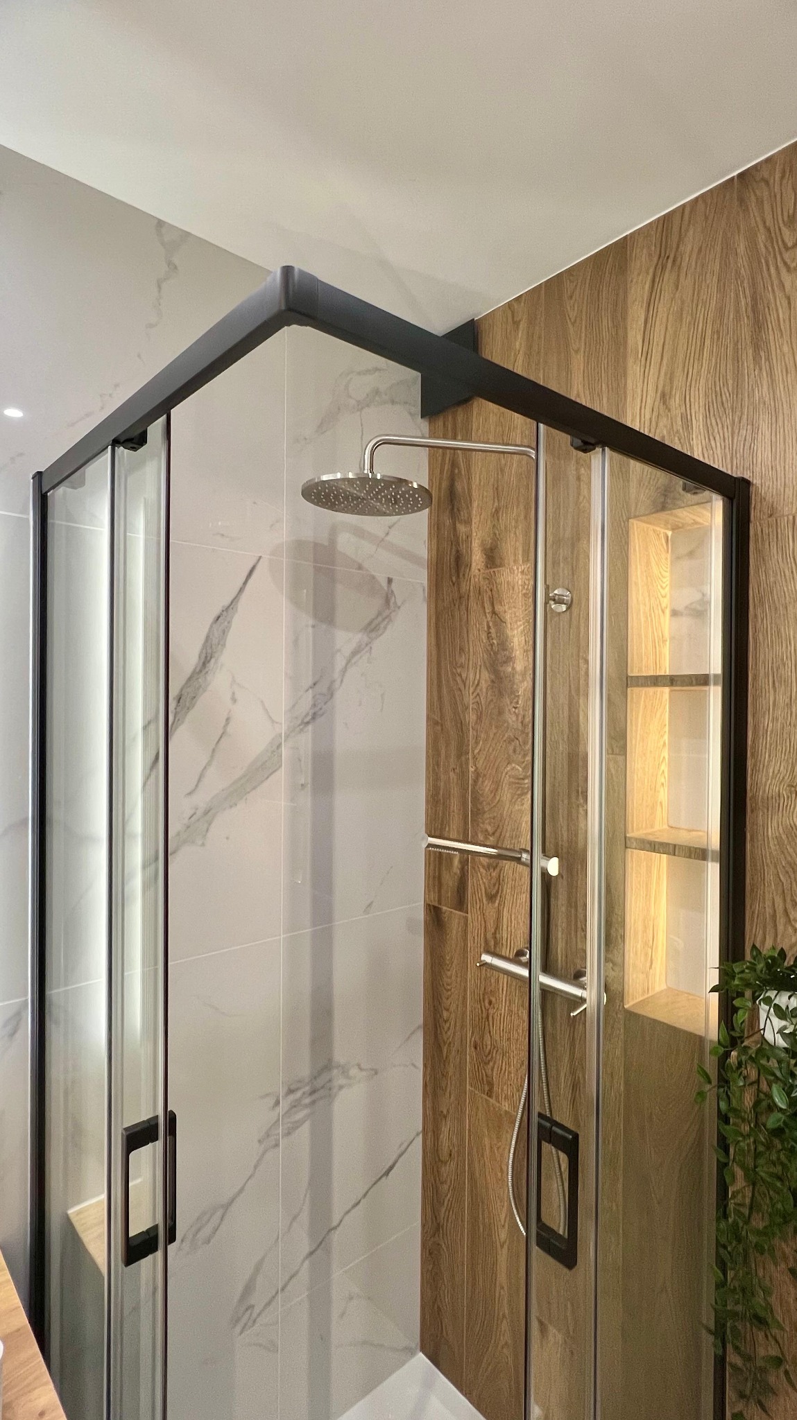 Nowoczesna kabina prysznicowa z czarnymi ramami, deszczownicą i drewnopodobnymi płytkami w aranżacji łazienki. Widoczne detale wykończenia.