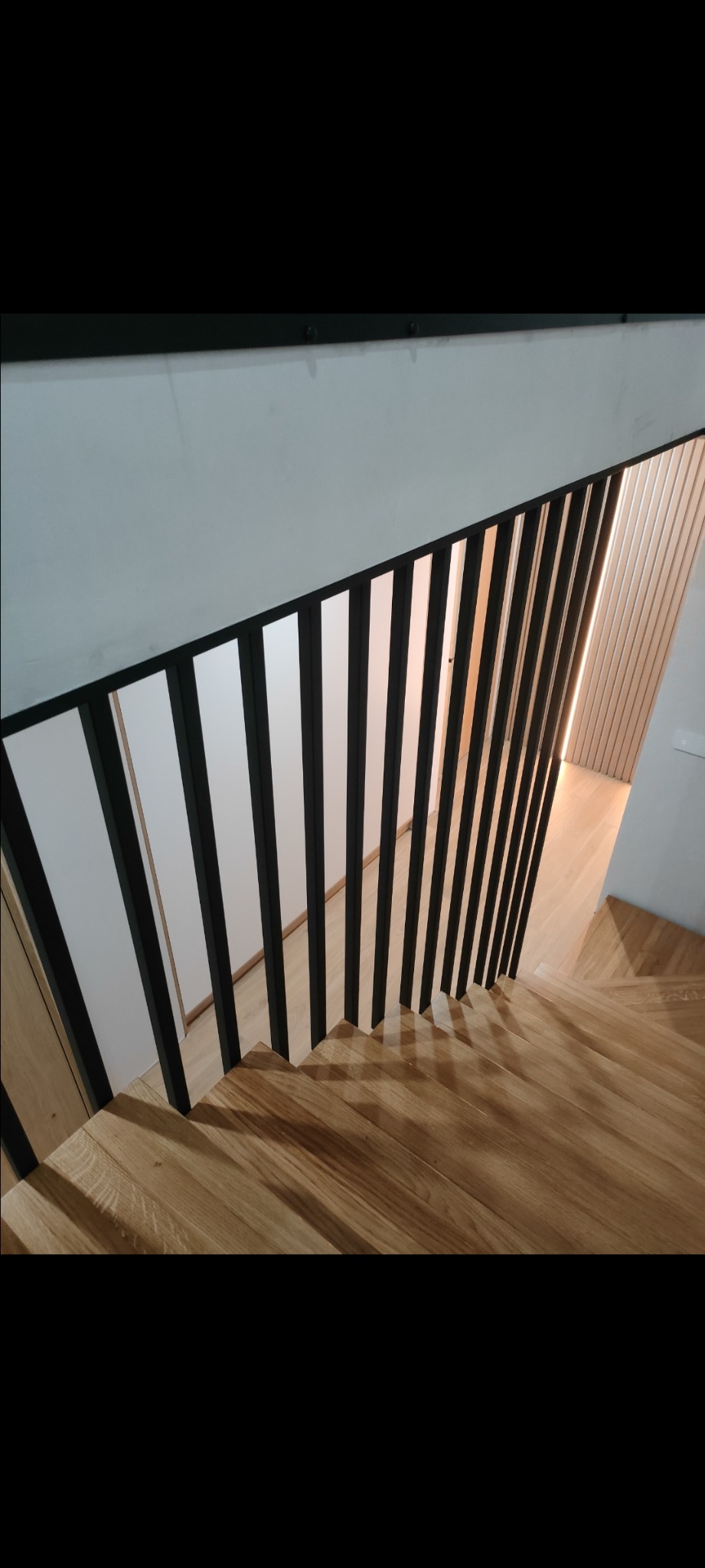 Drewniane schody z czarnymi, pionowymi słupkami balustrady, widok z góry, jasne wnętrze.