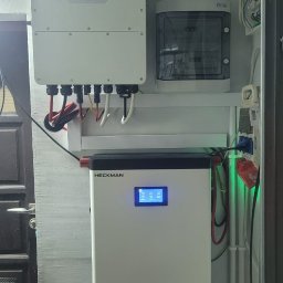 Liqene Fotowoltaika Radom, Pompy Ciepła - Zamontowany magazyn energii Heckman z wyświetlaczem LCD, obok skrzynka elektryczna i falownik Deye. Widoczne kable i przewody. Całość zamontowana na ścianie wewnątrz budynku.