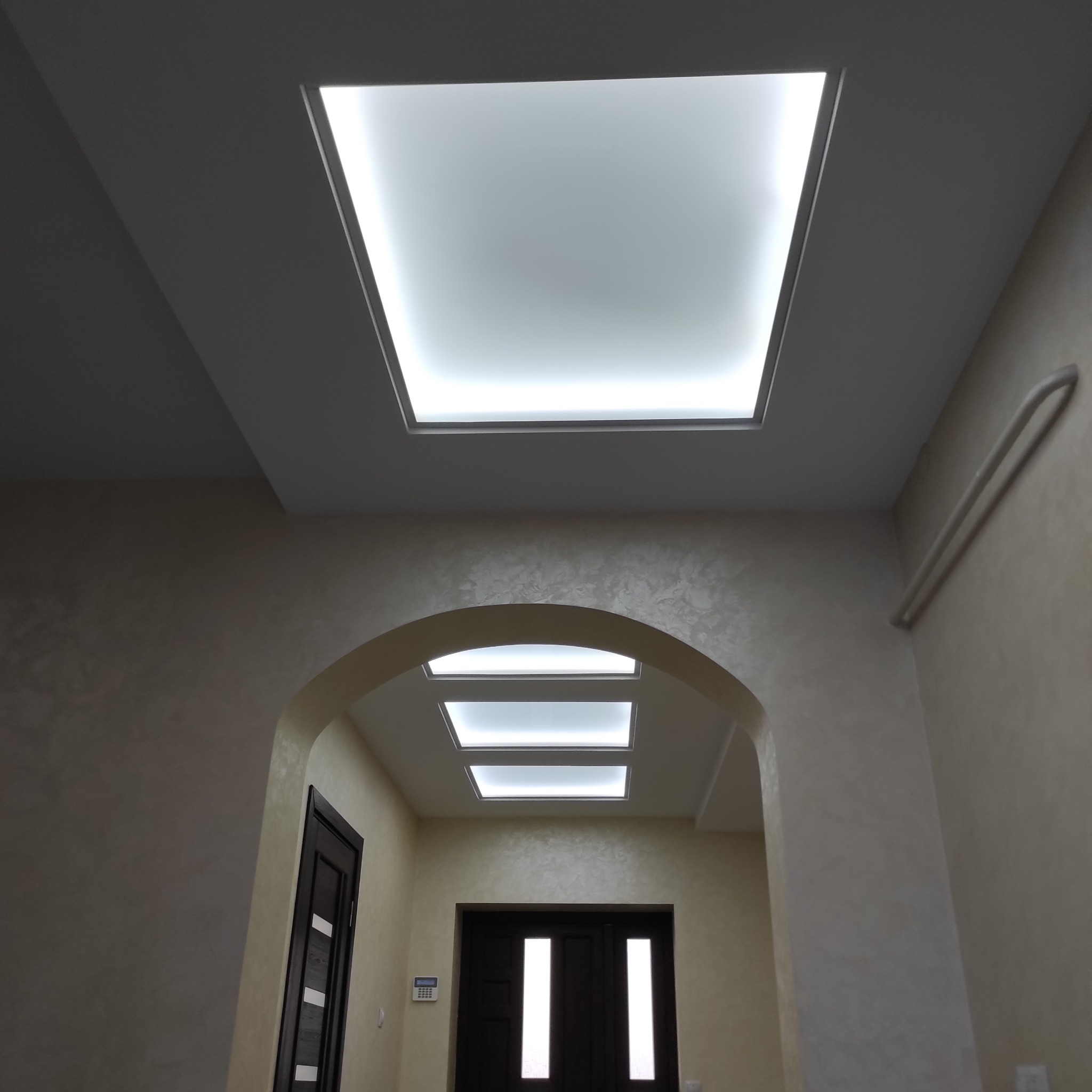 Nowoczesne oświetlenie sufitowe w korytarzu z łukowatym przejściem i dekoracyjną fakturą ścian.