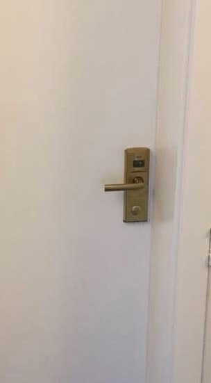 Złoty, elektroniczny zamek z klamką na białych drzwiach wewnętrznych, widoczne niewielkie cyfrowe okienko na zamku.