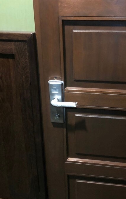 Brązowe drzwi z zamkiem elektronicznym, którego klamka jest owinięta białą taśmą.