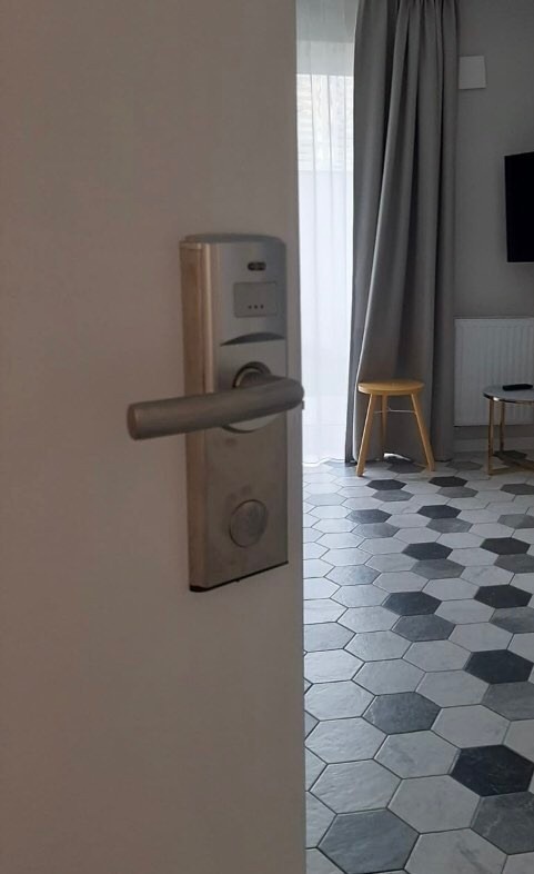 Elektroniczny zamek w drzwiach wejściowych do mieszkania, widoczny fragment wnętrza z krzesłami i heksagonalną podłogą.