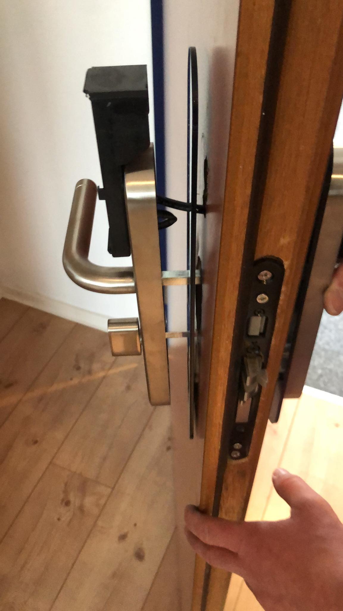 Montaż zamka elektronicznego w drewnianej ramie drzwi wejściowych, widoczne elementy mechanizmu i uchwyt ze stali nierdzewnej.