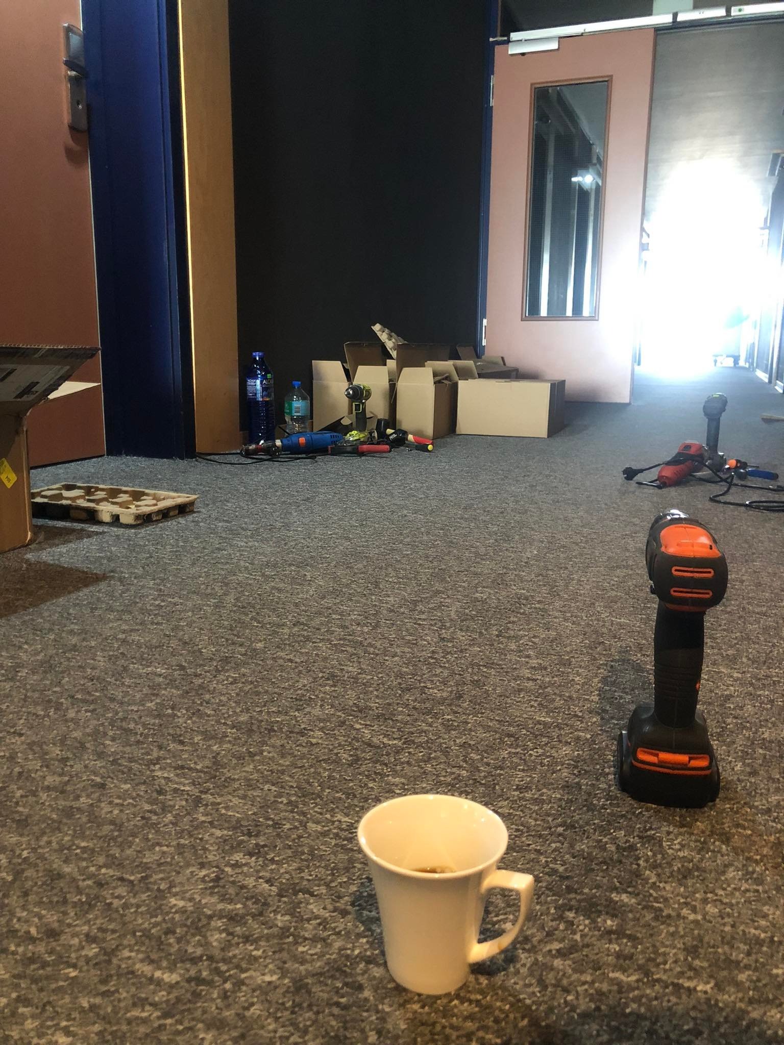 Rozstawione narzędzia, wiertarka i kubek z kawą na szarym dywanie w trakcie montażu drzwi.