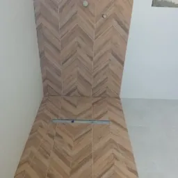 Ukończona łazienka z brązowymi płytkami ułożonymi w jodełkę na ścianie i podłodze, widoczny odpływ liniowy i przygotowane punkty pod armaturę.