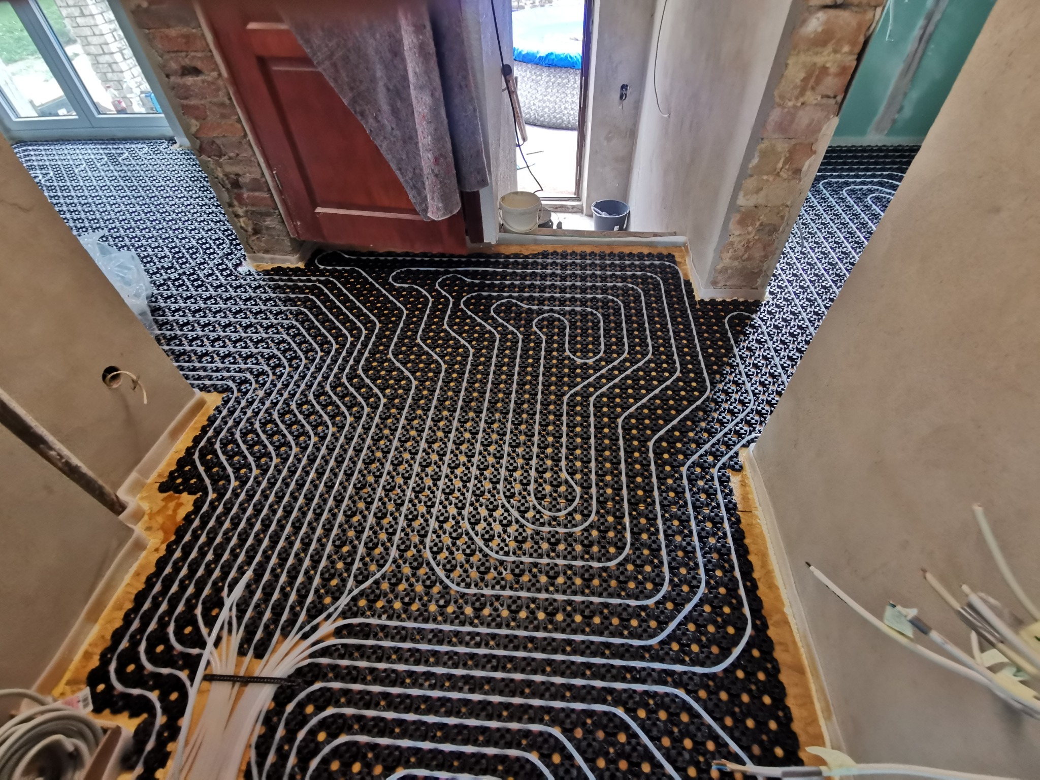 Rozłożona instalacja ogrzewania podłogowego na czarnej macie z żółtą izolacją, widok z góry, surowy stan wykończenia wnętrza.