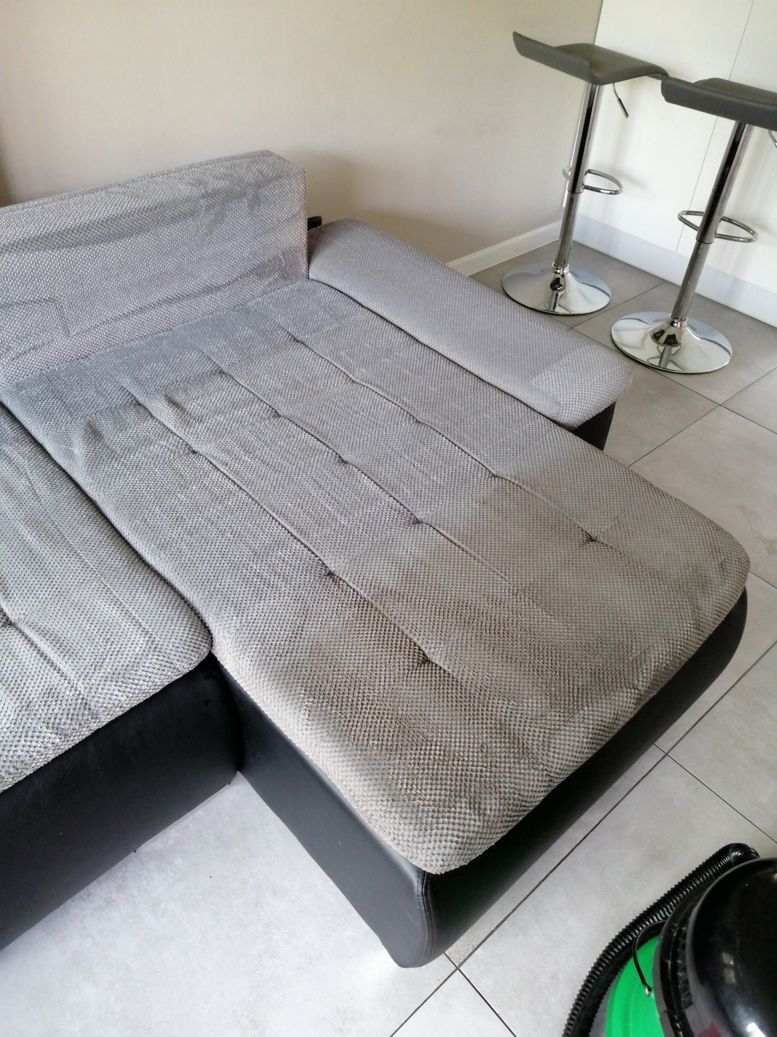 Szara, modułowa kanapa narożna z ciemnymi, skórzanymi bokami, widoczny fragment odkurzacza piorącego na podłodze z płytek.