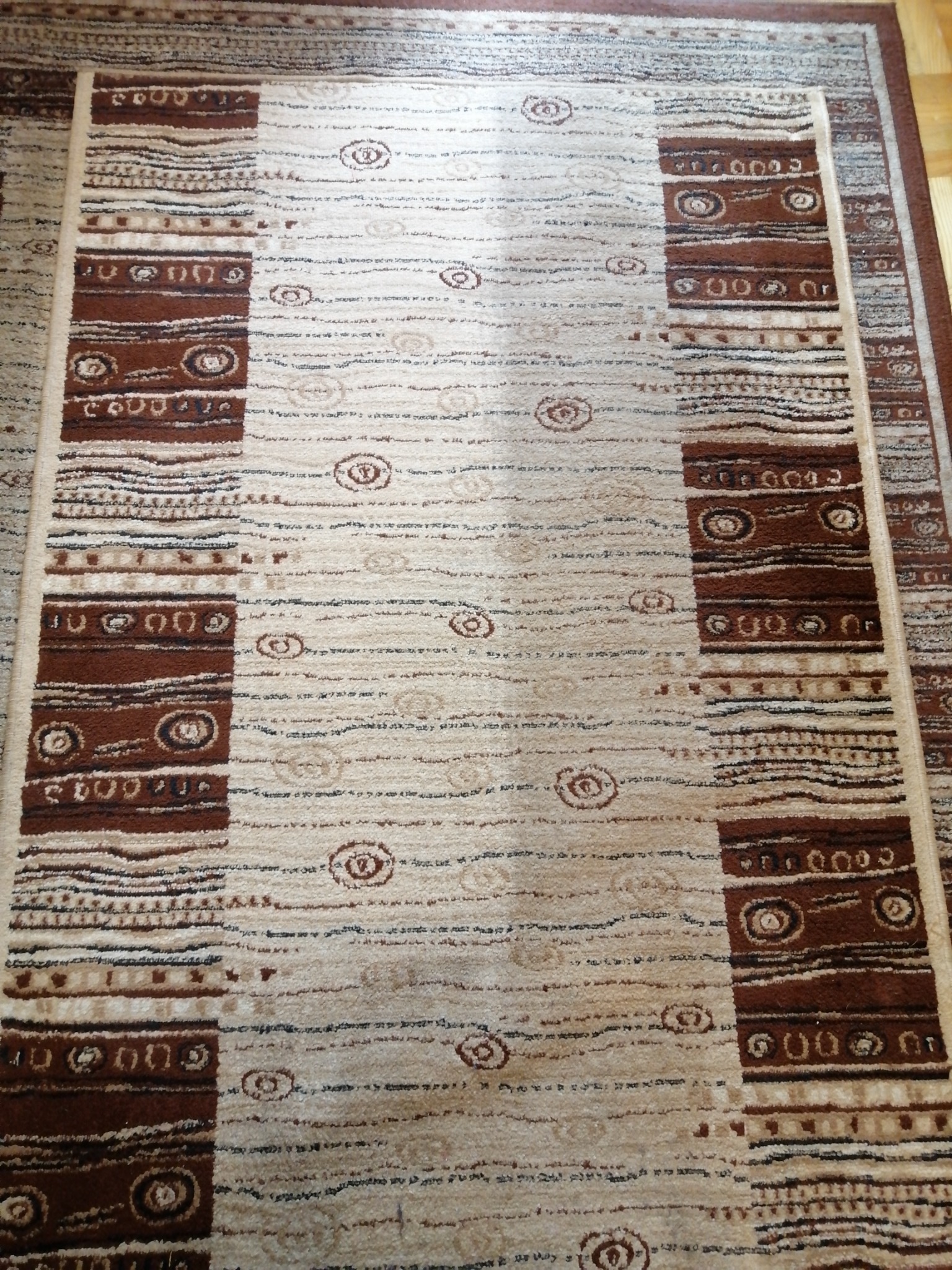 Beżowy dywan z brązowymi geometrycznymi wzorami, widoczne detale faktury i krawędzi.