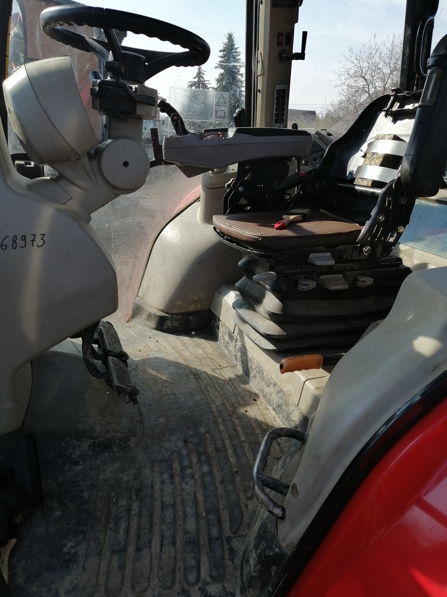 Wnętrze kabiny traktora z widocznym brudnym podłożem, pedałami, fotelem kierowcy i elementami sterowania.