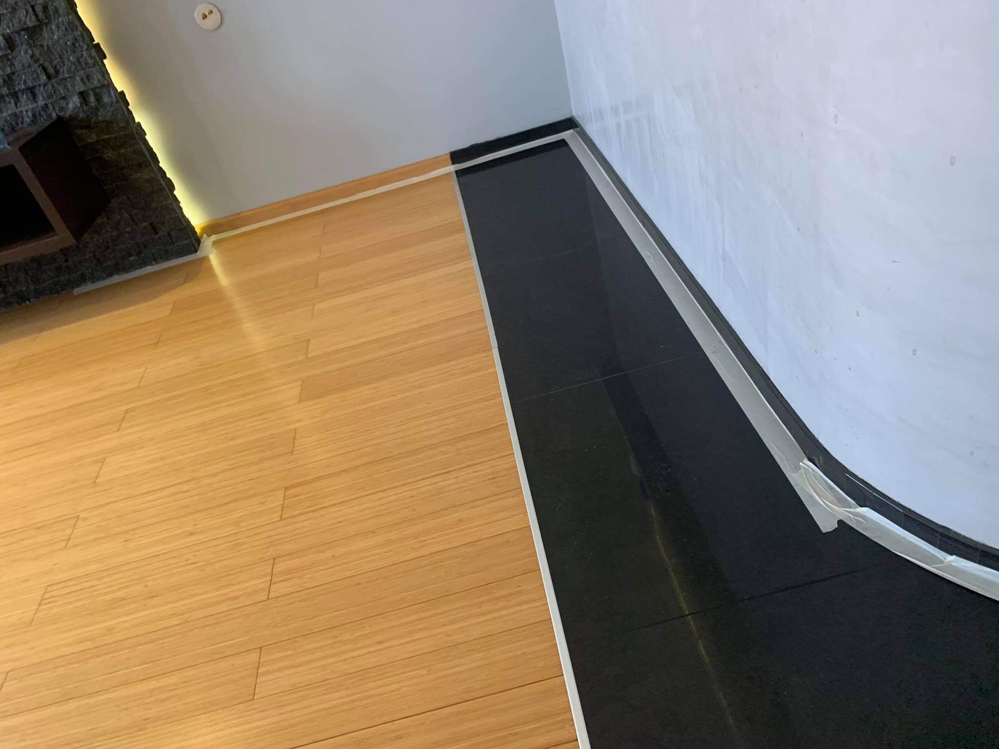 Połączenie jasnego parkietu i czarnych płytek podłogowych, zabezpieczone taśmą malarską przy ścianie, widok z góry.