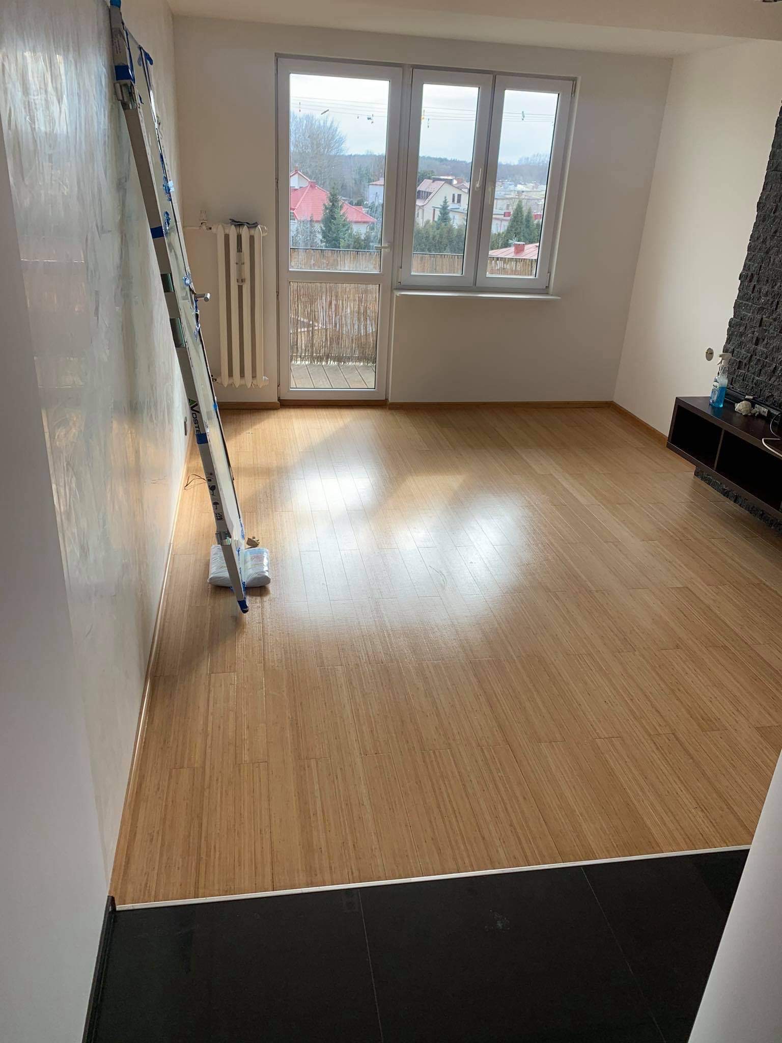 Pokój po remoncie z ułożoną jasną podłogą z paneli imitujących drewno; oparta o ścianę drabina malarska zabezpieczona folią.