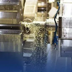 Obróbka metalu na tokarce CNC z chłodziwem, widoczne wióry i płyn chłodzący w ruchu, maszyna w kolorze szarym.