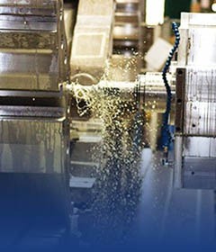 Obróbka metalu na tokarce CNC z chłodziwem, widoczne wióry i płyn chłodzący w ruchu, maszyna w kolorze szarym.