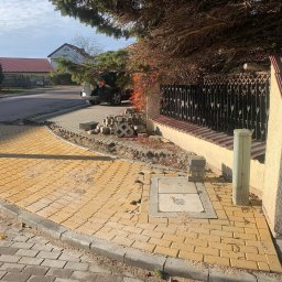 Wnortex Construction Sp. z o.o. - Żółta kostka brukowa ułożona na zakręcie chodnika, z widocznym włazem studzienki i przygotowanym miejscem na dalsze prace brukarskie przy ogrodzeniu.