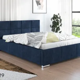 Tapicerowane łóżko w kolorze granatowym z pikowanym zagłówkiem, biała pościel w geometryczne wzory, okno z widokiem na zieleń, dywan w odcieniach brązu i bieli, napis 'ASTON 29' w lewym dolnym rogu.