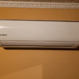 Biała jednostka wewnętrzna klimatyzatora Kaisai zamontowana na pomarańczowej ścianie z dekoracyjną listwą przysufitową.