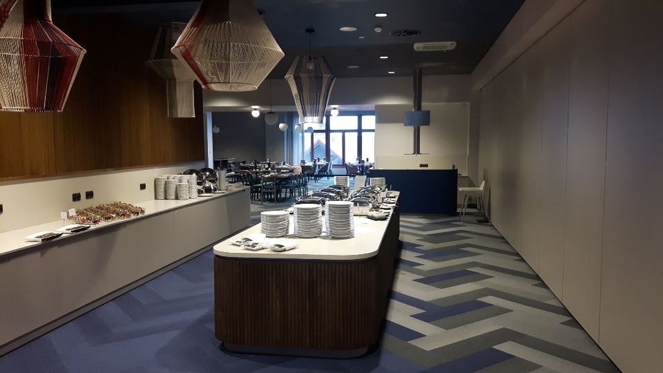 Wnętrze restauracji w Bielawie z niebieską wykładziną w geometryczny wzór i drewnianymi elementami wystroju.