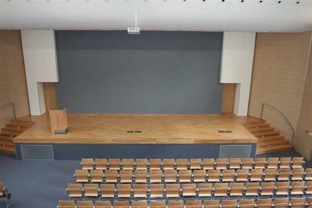 Sala konferencyjna z drewnianą podłogą, schodami i rzędami krzeseł, widok z góry.