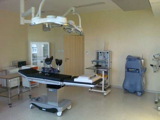 Sala operacyjna z nowoczesnym stołem operacyjnym, lampami sufitowymi i sprzętem medycznym, oświetlona neutralnym światłem.