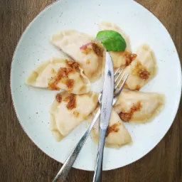 Porcja pierogów okraszonych smażoną cebulką, udekorowana listkiem zieleniny, podana na talerzu z widelcem i nożem w Gdańsku.