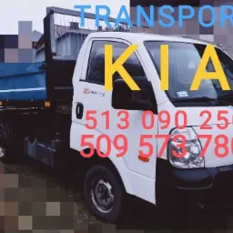 Biały samochód dostawczy marki KIA z otwartą skrzynią ładunkową, z naniesionymi numerami telefonów kontaktowych na karoserii.