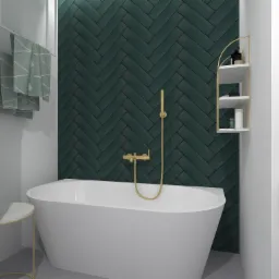 Minimalistyczna łazienka z białą wanną wolnostojącą, złotą armaturą na tle ściany wyłożonej ciemnozielonymi płytkami ułożonymi w jodełkę, oraz półką narożną z kosmetykami.