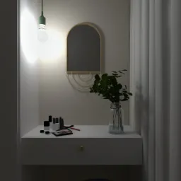 Toaletka z kosmetykami i lustrem w złotym obramowaniu, oświetlona wiszącą lampą z zielonym kablem, uzupełniona wazonem z zielonymi liśćmi, na tle zasłon.