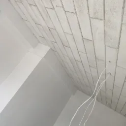 Wnętrze w trakcie wykończenia: sufit z płyt imitujących cegłę, białe ściany, wystające przewody elektryczne.