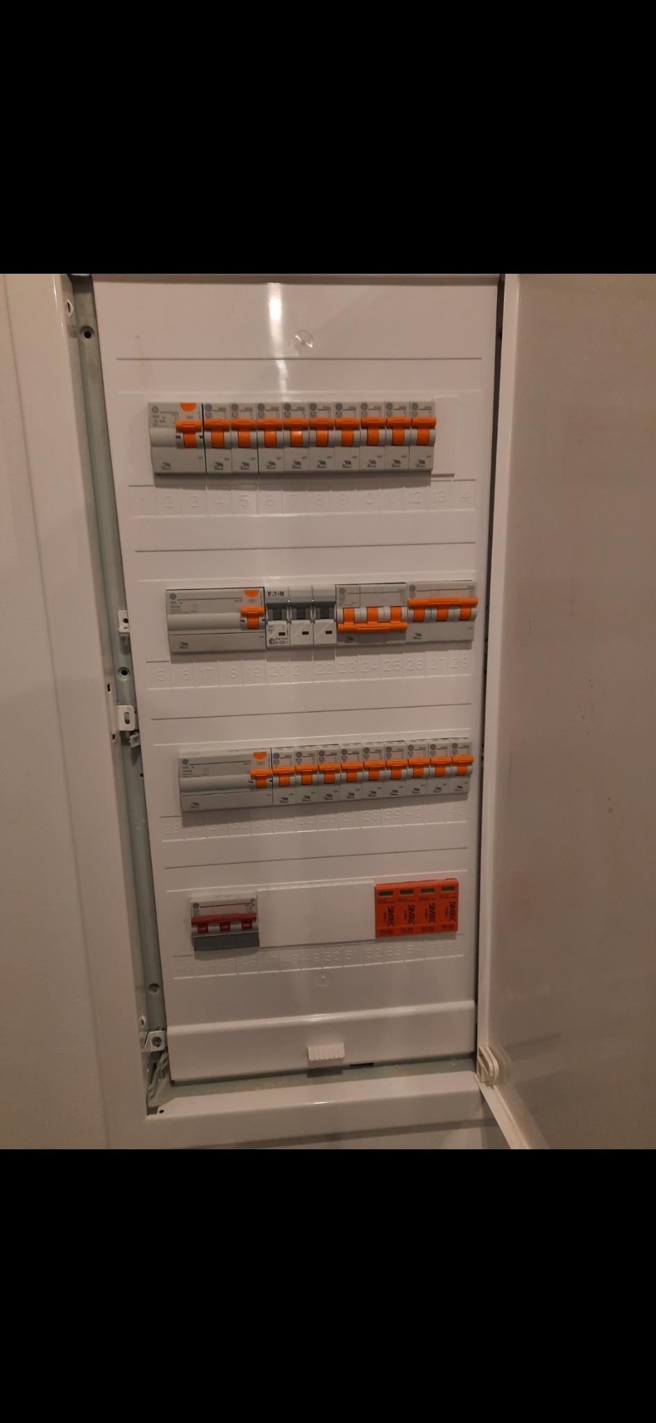 Otwarta, biała skrzynka rozdzielcza z bezpiecznikami Eaton i Sharak, widoczne numery obwodów.