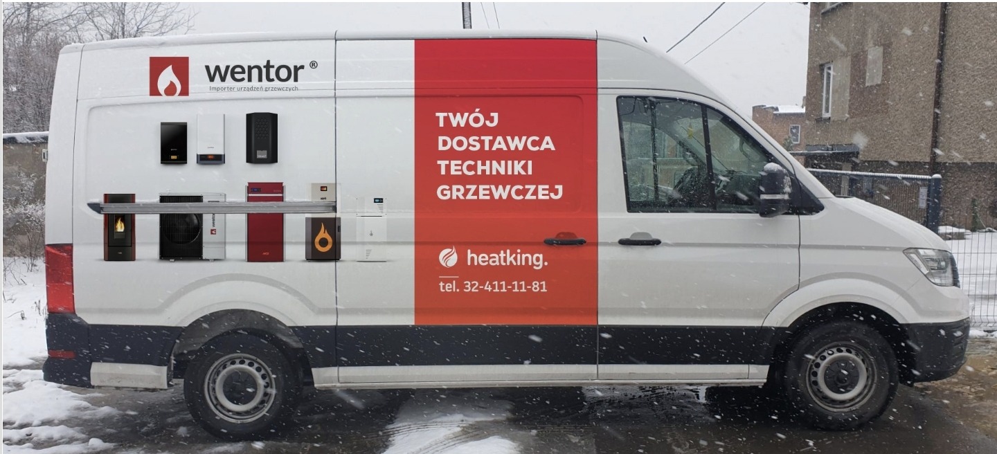 Biały samochód dostawczy z reklamą importera urządzeń grzewczych, prezentujący różne modele kotłów i pieców na boku, z logo 'Wentor' i 'Heatking' oraz numerem telefonu, sfotografowany w zimowej...