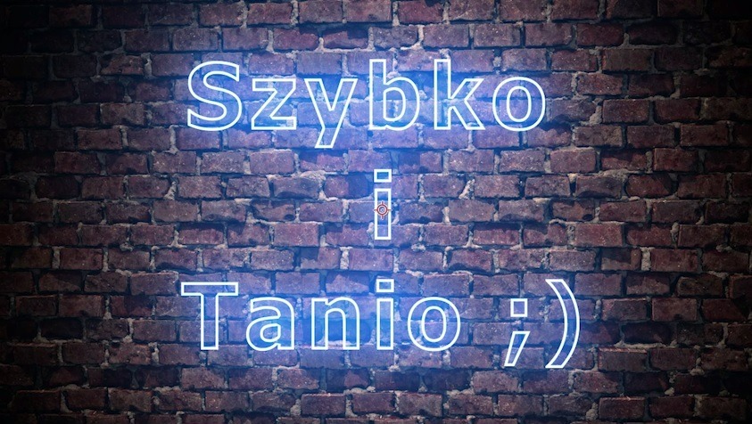 Neonowy napis 'Szybko i Tanio ;)' na tle ceglanej ściany.