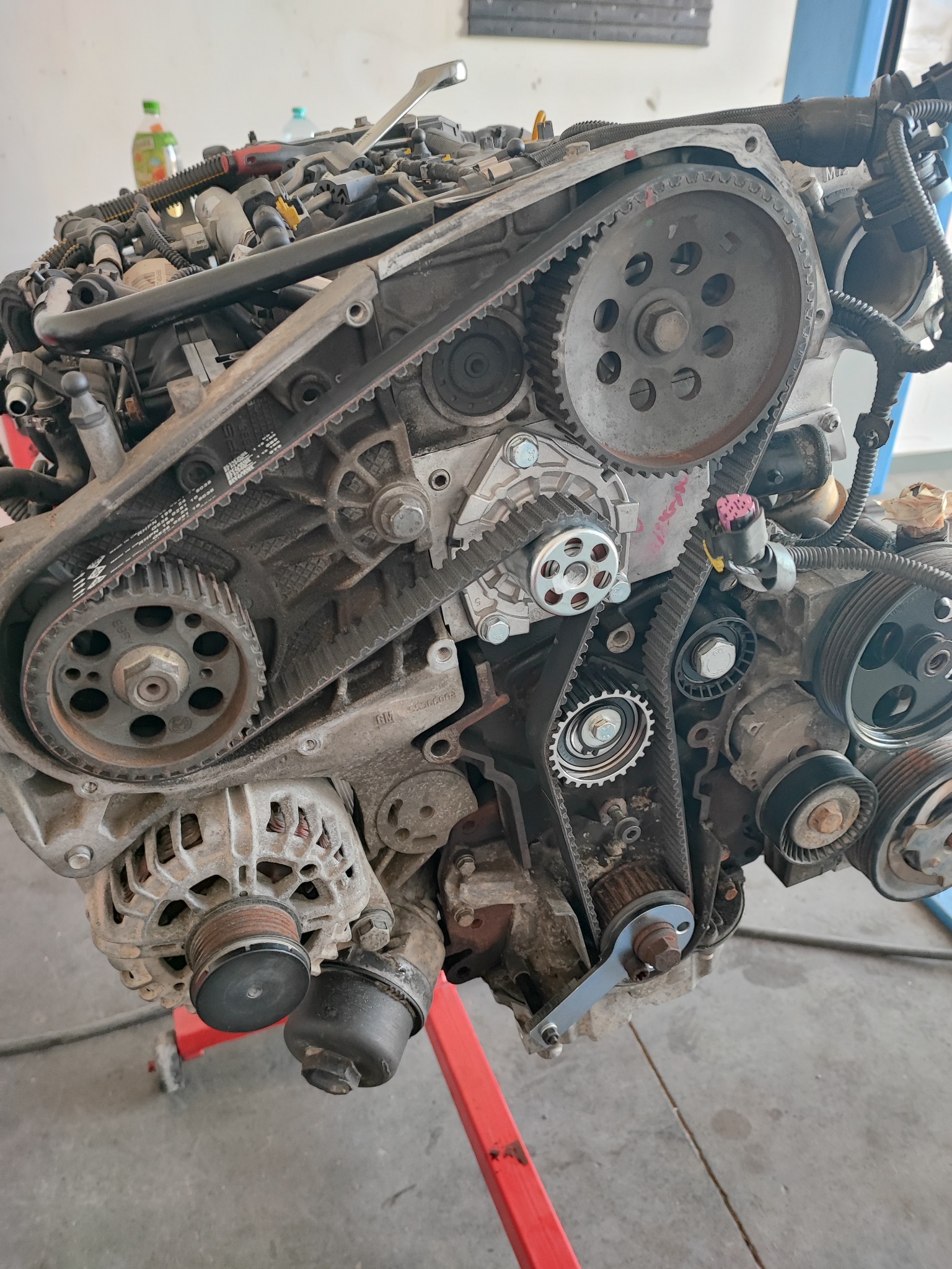 Zdemontowany silnik samochodowy z widocznymi paskami rozrządu i kołami pasowymi, umieszczony na stojaku w warsztacie w Chrząstowicach. Widoczne ślady użytkowania i zabrudzenia na elementach.