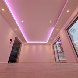 BauTech - Nowoczesne wnętrze z podświetlanym sufitem LED w kolorze różowym, widok na zewnątrz przez duże okna, częściowo widoczny samochód dostawczy w przejściu.