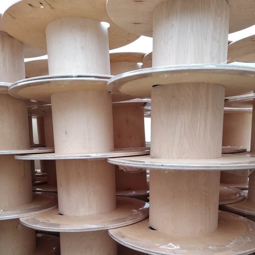 Stos drewnianych szpul na kable, widoczne słoje drewna i plastikowa folia zabezpieczająca.