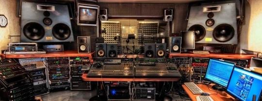 Profesjonalne studio nagrań z mikserem, monitorami studyjnymi, komputerami i panelami akustycznymi na ścianach.