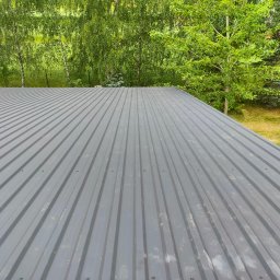 Perium Marek Ożga - Szary dach z blachy trapezowej, widok z góry na tle zieleni drzew i pola. Nowoczesne pokrycie dachowe.